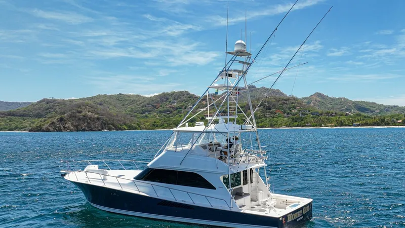 Slide: The Image of Profile View of Viking 61 Convertible This image showcases the sleek profile of the 2005 Viking 61 Convertible, 'Honey Girl'. The vessel features a spacious aft deck designed for fishing or leisure, complemented by a robust tower with multiple observation levels. Its classic lines and polishe - 6449606