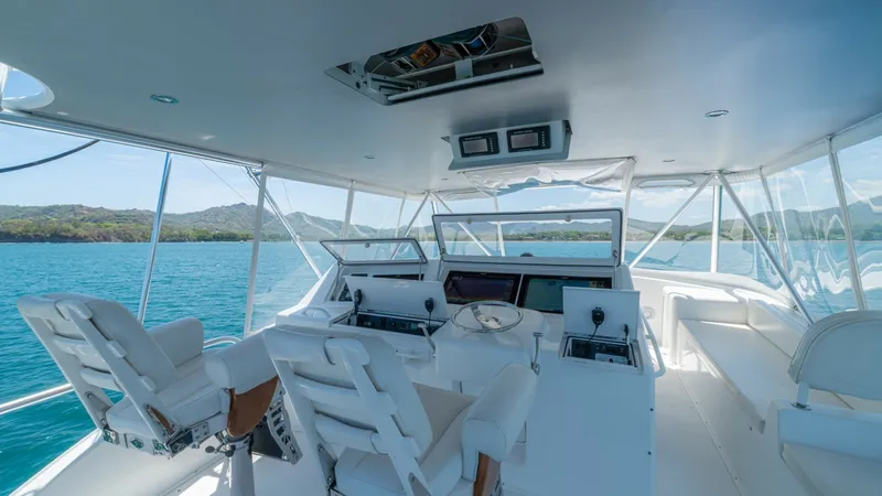 Slide: The Image of Flybridge Helm Station View The flybridge of the 2005 Viking 61 Convertible 'Honey Girl' offers a commanding view with its dual helm chairs and state-of-the-art navigation equipment. The open design features ample seating, allowing for both functionality and comfort while cruising. - 6449564
