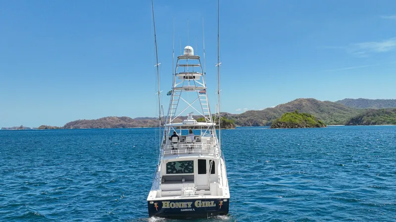 Slide: The Image of Aft View with Tower and Nameplate This image showcases the striking aft view of the 2005 Viking 61 Convertible, 'Honey Girl,' emphasizing its robust tower structure designed for optimal fishing and navigation. The vessel's nameplate is prominently displayed, highlighted by a sleek design - 6449607