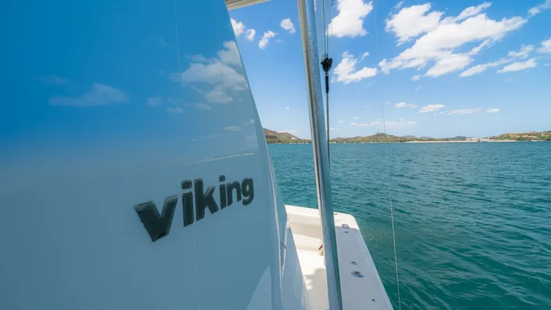 Slide: The Image of Starboard Side with Viking Branding This image showcases the starboard side of the 2005 Viking 61 Convertible, prominently featuring the distinctive Viking logo against the sleek, polished hull. The view captures the vessel's seamless finish and attention to detail, set against a stunning b - 6449576