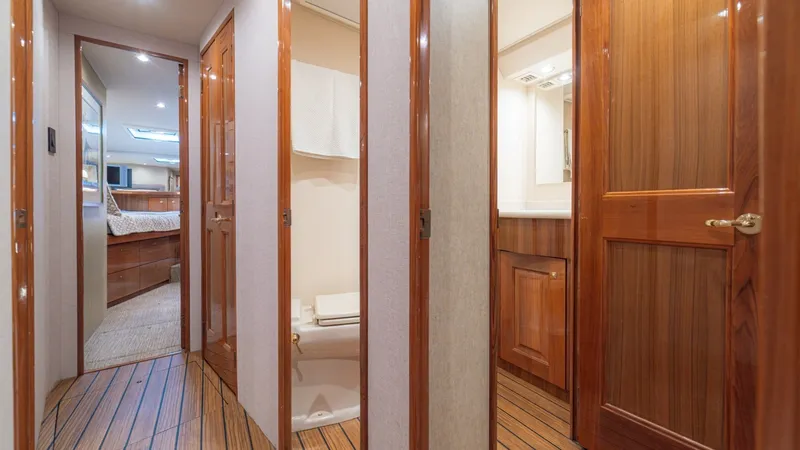 Slide: The Image of Hallway Leading to Stateroom and Head This image showcases a sleek hallway on the Viking 61 Convertible, featuring rich wood finishes and elegant lighting. The corridor leads to a spacious stateroom and a well-appointed head, both designed for comfort and luxury. The teak flooring adds warmth - 6449530
