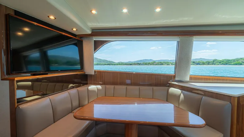 Slide: The Image of Spacious Salon Dinette Area The salon of the 2005 Viking 61 Convertible features a cozy dinette area with plush, wrap-around seating and a polished wooden table, perfect for dining or entertaining. Large windows provide panoramic views and natural light, enhancing the inviting atmos - 6449519
