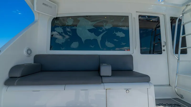 Slide: The Image of Cockpit Seating Area with Window Art This image showcases the cockpit seating area of the 2005 Viking 61 Convertible, featuring a sleek, cushioned bench for comfortable relaxation. The window behind the seating is adorned with artistic marine life etchings, adding a unique and stylish touch - 6449555