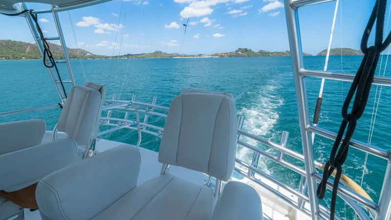 Slide: The Image of Flybridge Seating with Ocean View The flybridge of the 2005 Viking 61 Convertible 'Honey Girl' offers plush seating with stunning panoramic views of the open sea. The white cushioned chairs provide comfort for navigating or relaxing while enjoying the surroundings. The stainless steel rai - 6449563