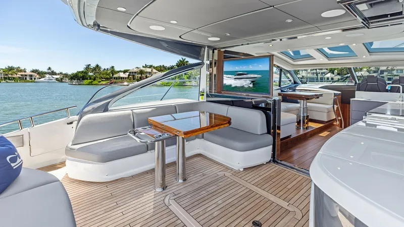 Slide: The Image of Spacious Cockpit Deck with Seating The Cockpit deck of the 2026 PRINCESS V55 offers an inviting space with plush, wraparound seating and a sleek wooden table, perfect for alfresco dining. The area is complemented by high-quality teak flooring and a retractable sunroof, allowing for an open - 6312333