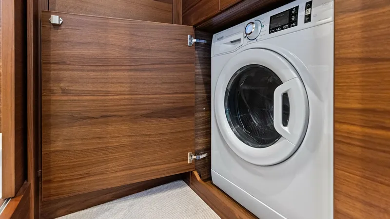 Slide: The Image of Hidden Laundry Appliance Area This image showcases a cleverly concealed laundry area on the 2026 Princess V55, featuring a modern washer neatly integrated behind a sleek wooden cabinet. The rich wood finish adds a touch of elegance, seamlessly blending functionality with style. Ideal - 6312350