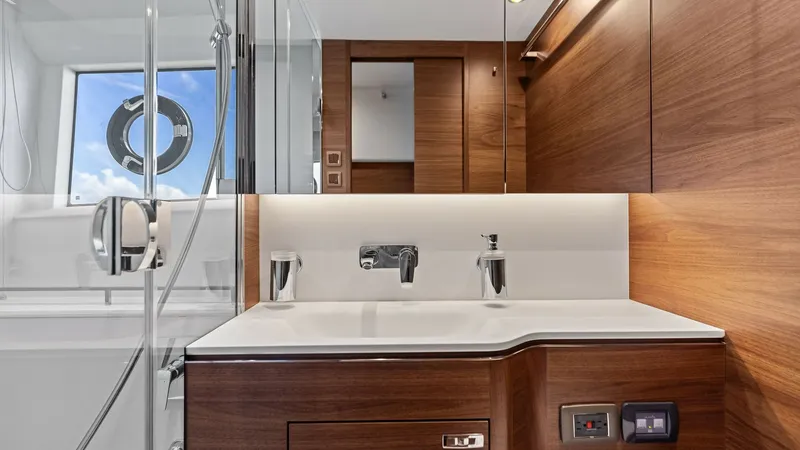 Slide: The Image of Luxurious Master En-Suite Bathroom The 2026 PRINCESS V55 features a sleek Master en-suite bathroom with contemporary wooden cabinetry and a modern dual-sink vanity. Elegant fixtures and ambient lighting complement the sophisticated design, while the window provides natural light and a view - 6312351
