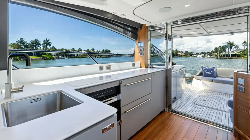 Slide: The Image of Galley and Aft Deck View This image showcases the sleek galley of the 2026 PRINCESS V55, featuring modern appliances and elegant cabinetry. The open layout seamlessly connects to the aft deck, offering stunning water views through large sliding glass doors. The combination of nat - 6312325