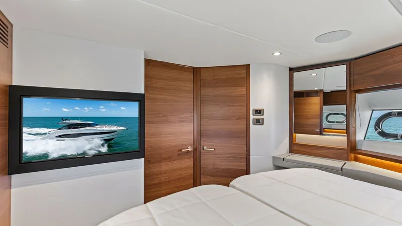 Slide: The Image of Luxurious VIP Stateroom with TV The VIP Stateroom of the 2026 PRINCESS V55 exudes elegance with its sleek design and high-quality finishes. The room features a plush double bed, rich wood accents, and ample storage, creating a cozy yet sophisticated atmosphere. A mounted flat-screen TV - 6312355