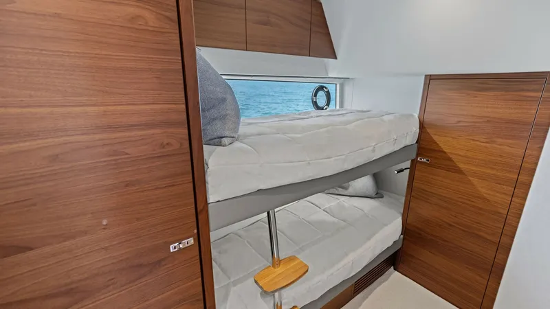 Slide: The Image of Guest Cabin with Bunk Beds This inviting guest cabin aboard the 2026 Princess V55 features cozy bunk beds, ideal for accommodating additional guests. The warm wood finishes and soft lighting create a comfortable and welcoming atmosphere. A large window provides natural light and of - 6312359