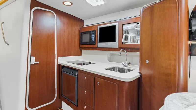 Slide: The Image of Galley with Modern Amenities The Wellcraft 360 Coastal's galley is equipped with sleek cabinetry and modern appliances, including a built-in microwave and stovetop. The polished wooden finish and ample counter space offer a blend of functionality and style. A stainless steel sink and - 6312503
