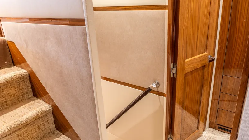 Slide: The Image of Interior Stairway and Hallway Entry This image showcases the elegant stairway and hallway entry aboard the 2020 Viking 92 Skybridge. The staircase features plush carpeting and sleek wood accents, leading to a beautifully crafted wooden door. The warm tones and quality finishes offer a welco - 6612531