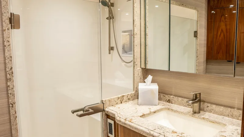 Slide: The Image of Luxurious Ensuite Bathroom This elegant ensuite bathroom on the 2020 Viking 92 Skybridge features a spacious glass-enclosed shower with modern fixtures. The vanity is adorned with a beautiful granite countertop, complemented by sleek cabinetry and ample mirror space. Warm wood fini - 6612530