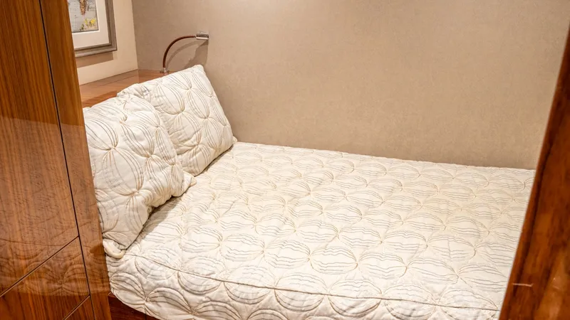 Slide: The Image of Guest Stateroom with Cozy Bedding This inviting guest stateroom on the Viking 92 Skybridge features a plush, quilted bed with matching pillows, providing a restful retreat. The warm wood tones and soft ambient lighting enhance the cozy atmosphere, while a stylish reading lamp offers addit - 6612532