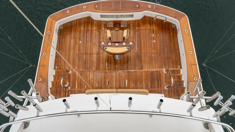 Slide: The Image of Aerial View of Aft Deck and Cockpit This image showcases the exquisite aft deck and cockpit of the Viking 92 Skybridge, featuring rich teak flooring and a well-appointed fighting chair. The spacious layout is ideal for fishing or entertaining, highlighted by rod holders and ample seating. T - 6612572