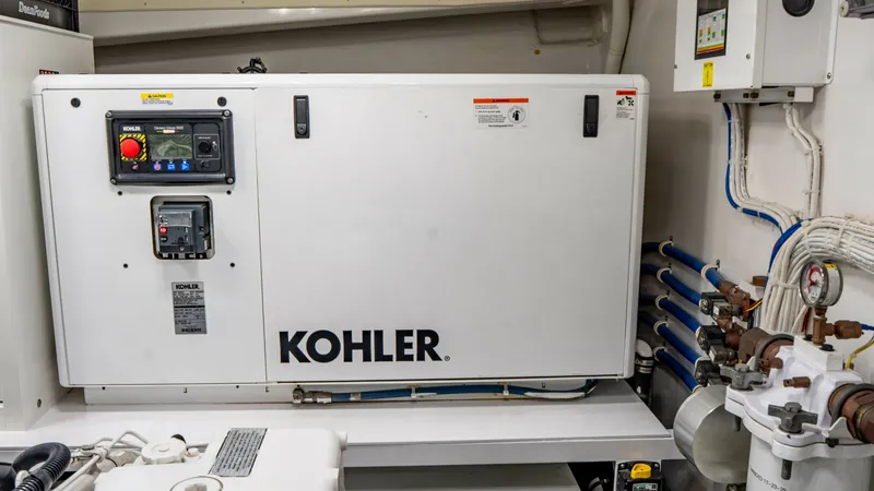 Slide: The Image of Engine Room with Kohler Generator This image showcases the engine room of the Viking 92 Skybridge, featuring a Kohler generator prominently installed. The area is well-organized, with neatly arranged piping and control systems ensuring optimal functionality. The clean and efficient design - 6612560