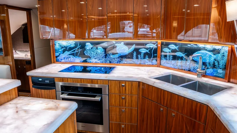 Slide: The Image of Elegant Galley with Custom Backsplash The galley of the vessel 'AFTER MIDNIGHT' showcases a sophisticated design with rich wood cabinetry and premium stainless steel appliances. The standout feature is the custom illuminated backsplash with an intricate marine design, adding a unique and arti - 6612513