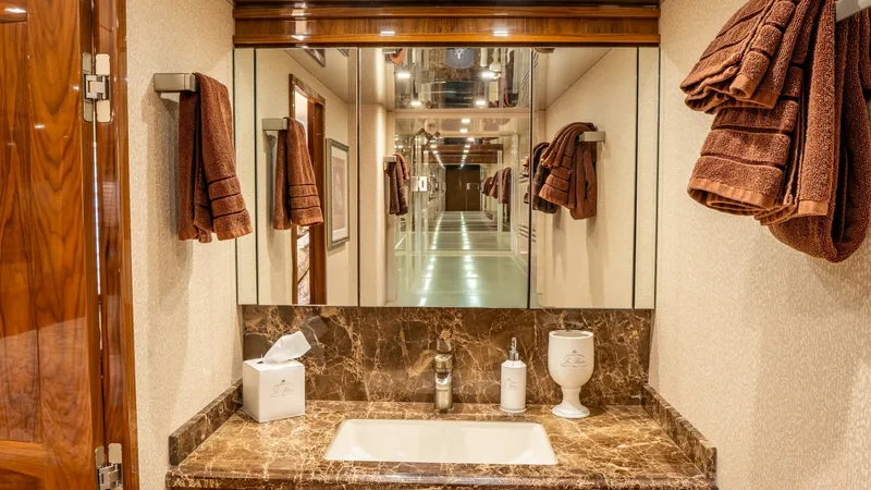 Slide: The Image of Luxurious Vanity in Guest Head This elegant guest head on the Viking 92 Skybridge features a beautifully crafted marble countertop and integrated sink. The warm wood finishes and mirrored cabinetry enhance the space, providing ample storage and a sophisticated aesthetic. Soft lighting - 6612544