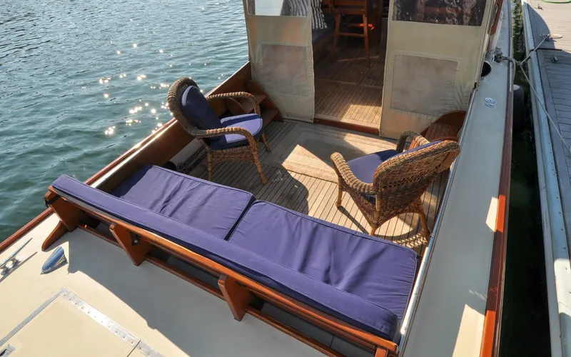 Slide: The Image of 1958 Bunker and Ellis 42 | Aleria 1958 Bunker and Ellis 42 boat deck with wicker chairs and blue cushions by the water. - 6307430