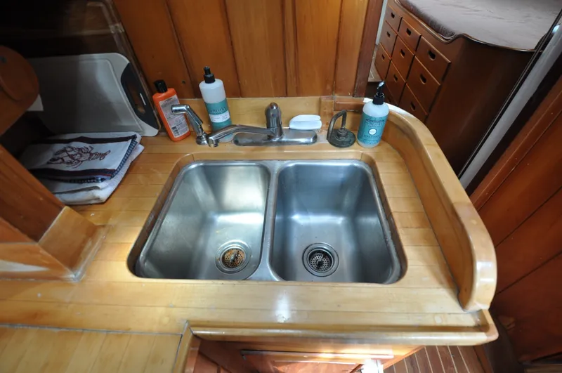 Slide: The Image of 1987 Wittholtz/Luzier 49 | Destiny Wooden boat kitchen sink with dual basins, soap, and cleaning supplies, 1987 Wittholtz/Luzier Sloop/Cutter. - 6319035