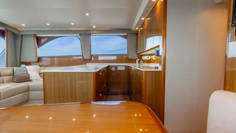 Slide: The Image of Elegant Salon with Galley View This Viking 45 Convertible's salon exudes warmth with its rich wood finishes and soft ambient lighting. The open layout seamlessly integrates the plush seating area and the well-appointed galley, featuring modern appliances and ample counter space. Large - 6394728