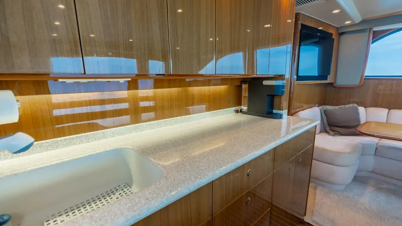 Slide: The Image of Galley with Polished Wood Finish The galley of the 2007 Viking 45 Convertible 'Desperado' showcases sleek, polished wood cabinetry complemented by a smooth, light-colored countertop. The area is well-lit, highlighting the ample storage space and modern sink. Adjacent to the galley, a coz - 6394735