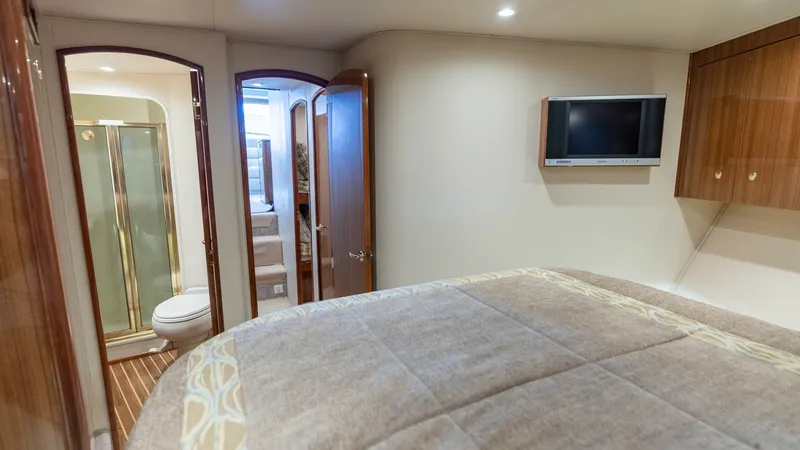 Slide: The Image of Master Stateroom with Ensuite Bathroom The master stateroom offers a spacious and inviting layout with a plush bed and direct access to the ensuite bathroom. Warm wood cabinetry provides ample storage, while the mounted flat-screen TV adds a touch of modern convenience. The ensuite bathroom fe - 6394739