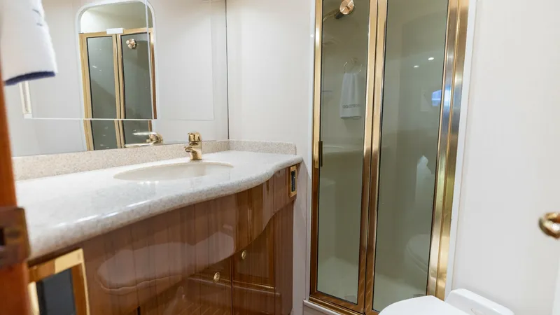 Slide: The Image of Luxurious En-Suite Bathroom This elegant en-suite bathroom on the 2007 Viking 45 Convertible features a spacious shower with a gold-tone frame, adding a touch of luxury. The vanity is topped with a polished stone countertop, complemented by high-gloss wood cabinetry for ample storag - 6394740