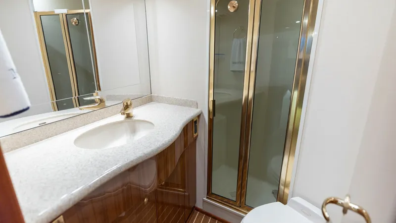 Slide: The Image of Elegant Ensuite Bathroom This well-appointed ensuite bathroom features a sleek glass-enclosed shower with gold accents that complement the elegant fixtures and fittings. The polished wooden cabinetry provides ample storage beneath a smooth, solid-surface countertop and integrated - 6394741