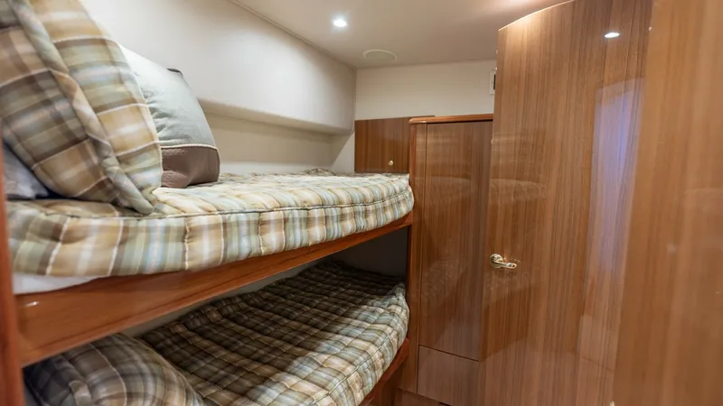 Slide: The Image of Guest Cabin with Bunk Beds This cozy guest cabin on the 2007 Viking 45 Convertible features neatly arranged bunk beds with plaid-patterned bedding, offering a comfortable and inviting space for guests. The high-gloss wooden cabinetry provides ample storage and adds a touch of elega - 6394743