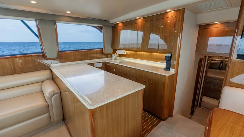 Slide: The Image of Galley and Salon View This inviting galley on the 2007 Viking 45 Convertible 'Desperado' features elegant wood cabinetry and a polished countertop, offering ample space for meal preparation. The open layout seamlessly connects to the salon, which is enhanced by large windows p - 6394723