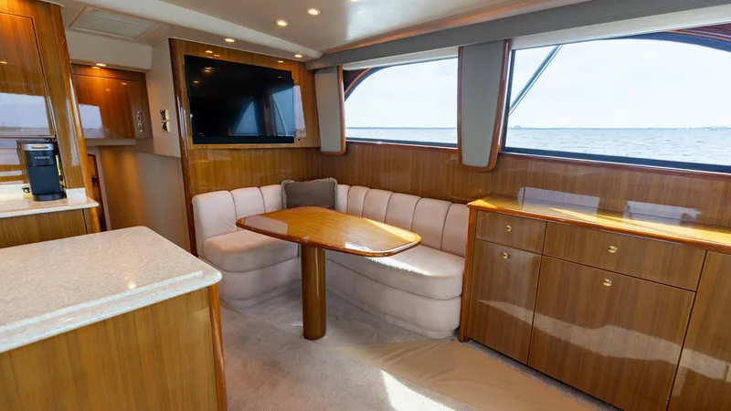 Slide: The Image of Spacious Salon with Dining Area The salon of the 2007 Viking 45 Convertible offers a welcoming and luxurious space with its elegant wood finishes and plush seating. A large, curved settee surrounds a polished dining table, providing an ideal setting for meals or relaxation. Natural ligh - 6394724