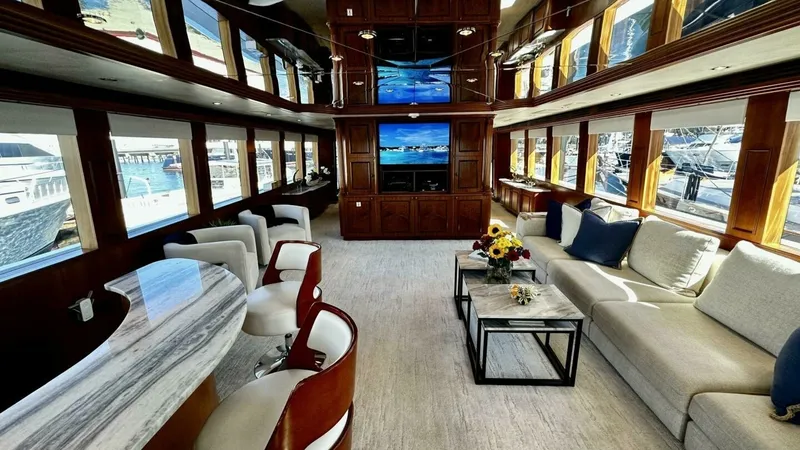 Slide: The Image of Spacious Salon with Entertainment Center The salon of the 2003 Hatteras Raised Pilothouse exudes luxury with its expansive layout and elegant finishes. Large windows provide panoramic views and natural light, enhancing the warm wood cabinetry and plush seating. A prominent entertainment center w - 6388376