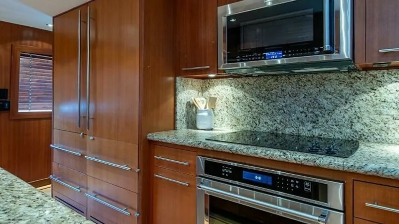 Slide: The Image of Galley Kitchen with Modern Appliances The galley of the 2003 Hatteras Raised Pilothouse showcases sleek wood cabinetry and modern stainless steel appliances, including a built-in microwave and oven. The granite countertops and backsplash add a touch of elegance and practicality, enhancing the - 6388389