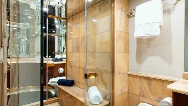 Slide: The Image of Luxurious Ensuite Bathroom This elegant ensuite bathroom features rich marble finishes and a spacious glass-enclosed shower, creating a sense of luxury and comfort. The warm hues of the tiles complement the polished wood cabinetry and gold accents, adding sophistication to the spac - 6388396