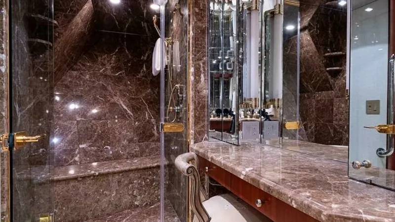 Slide: The Image of Luxurious Marble Ensuite Bathroom This opulent ensuite bathroom features exquisite marble finishes throughout, providing a sense of luxury and sophistication. The spacious shower area boasts glass enclosures and gold-toned accents, complementing the rich tones of the marble. A plush seati - 6388402