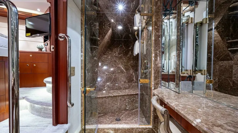 Slide: The Image of Luxurious Marble Bathroom with Shower This elegant bathroom features exquisite marble surfaces, including a spacious walk-in shower with glass doors and gold accents, offering a luxurious bathing experience. The mirrored walls enhance the sense of space and light, while the rich wood cabinetr - 6388403
