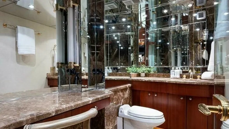Slide: The Image of Luxurious Yacht Bathroom Interior This opulent yacht bathroom features elegant marble countertops and rich wood cabinetry, creating a sophisticated ambiance. The space is enhanced by mirrored walls that reflect light, adding to the room's spacious feel. Gold-toned fixtures and plush ameni - 6388405