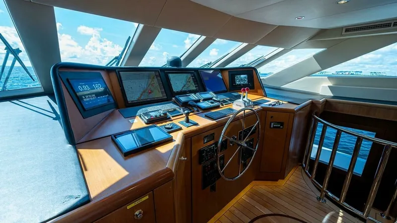 Slide: The Image of Sophisticated Raised Pilothouse Helm Station The helm station of the 2003 Hatteras Raised Pilothouse offers an expansive view through large panoramic windows, providing excellent visibility. Equipped with advanced navigation systems, multiple displays, and a classic wooden steering wheel, this helm - 6388417