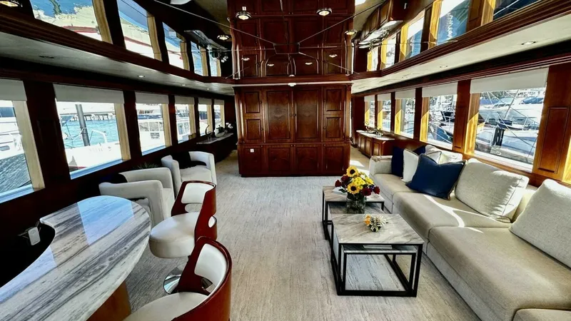 Slide: The Image of Spacious Salon with Panoramic Windows This elegant salon on the Hatteras Raised Pilothouse offers a luxurious and inviting atmosphere, featuring large panoramic windows that flood the space with natural light. The area is tastefully furnished with plush seating and a stylish marble-topped bar - 6388380