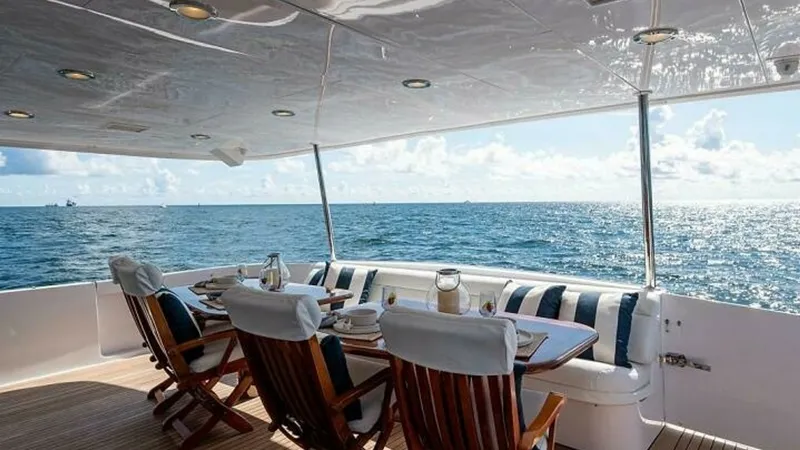 Slide: The Image of Aft Deck Dining Area This inviting aft deck of the 2003 Hatteras Raised Pilothouse features a spacious outdoor dining area with elegant teak chairs and a plush cushioned bench. The area is beautifully set for al fresco dining, offering stunning panoramic ocean views. The over - 6388436