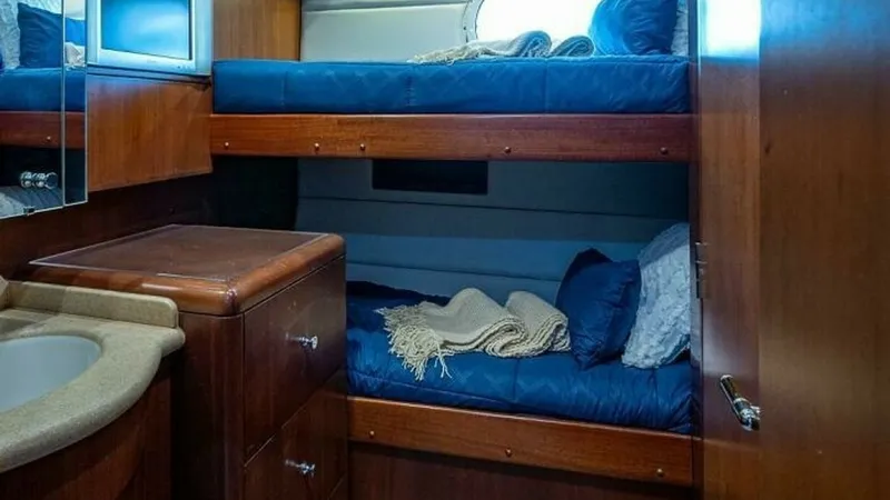 Slide: The Image of Cozy Twin Bunk Cabin Interior This inviting twin bunk cabin features rich wood paneling and plush blue bedding, creating a warm and comfortable atmosphere. A compact, yet functional layout includes a built-in storage cabinet and a small vanity with a sleek countertop. The soft lightin - 6388443