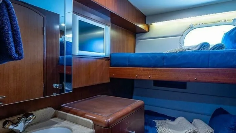Slide: The Image of Cozy Guest Cabin with Bunks This inviting guest cabin features comfortable bunk beds adorned with plush blue bedding, perfect for restful nights at sea. Warm wood paneling and cabinetry provide ample storage while enhancing the cabin's cozy ambiance. A compact sink area with a mirro - 6388444