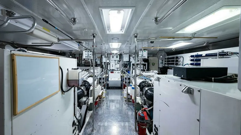 Slide: The Image of Engine Room with Twin Engines The engine room of the 2003 Hatteras Raised Pilothouse features a spacious layout with twin engines, providing ample space for maintenance and operations. Bright overhead lighting and a clean, organized environment enhance the functionality. The metallic - 6388451