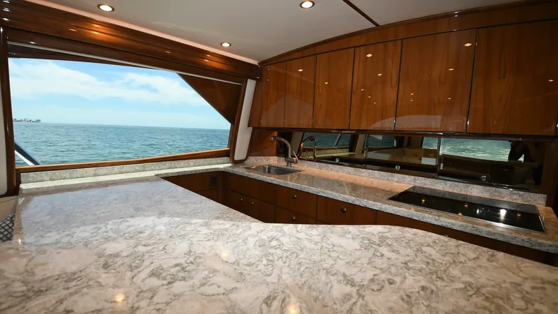 Slide: The Image of Galley with Ocean View The elegant galley of the 2020 Viking 58 Convertible features sleek wooden cabinetry and expansive countertops, providing ample space for meal preparation. Large windows offer breathtaking ocean views, enhancing the open and airy feel of the space. Modern - 6388296