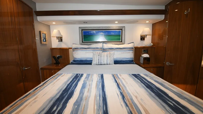 Slide: The Image of Master Stateroom with Queen Bed The master stateroom of the 2020 Viking 58 Convertible features a luxurious queen-size bed, highlighted by elegant wooden cabinetry. Ambient lighting and wall sconces create a warm and inviting atmosphere, while the artistic wall piece adds a touch of sop - 6388301
