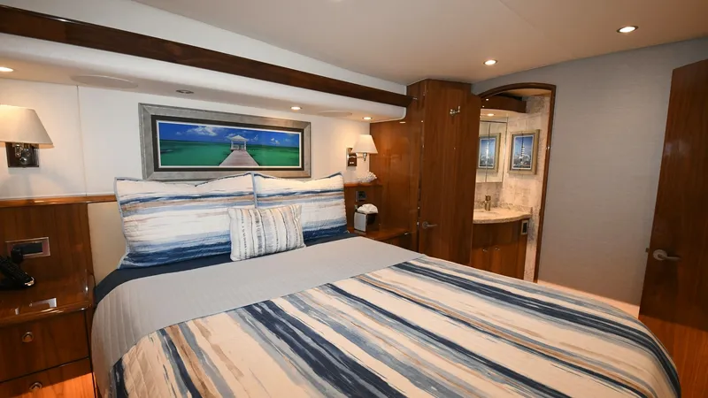 Slide: The Image of Master Stateroom with Ensuite The master stateroom offers a luxurious retreat with a spacious queen-sized bed adorned in nautical-themed linens. Rich wooden cabinetry and soft ambient lighting create a warm, inviting atmosphere. The ensuite bathroom, visible through the open door, fea - 6388302