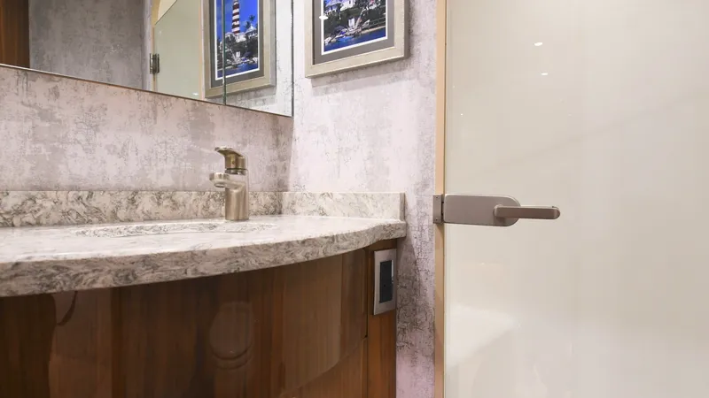Slide: The Image of Elegant Vanity in Guest Head This guest head features a beautifully crafted vanity with a polished stone countertop and modern fixtures. The light wood cabinetry complements the stylish wall finish, creating an inviting and sophisticated atmosphere. Framed artwork and a large mirror - 6388304