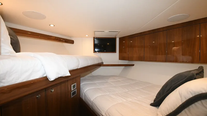 Slide: The Image of Guest Stateroom with Twin Berths This cozy guest stateroom on the 2020 Viking 58 Convertible features twin berths, perfect for accommodating extra passengers. The space is enhanced by rich wooden cabinetry and soft ambient lighting, creating a warm and inviting atmosphere. A built-in fla - 6388305
