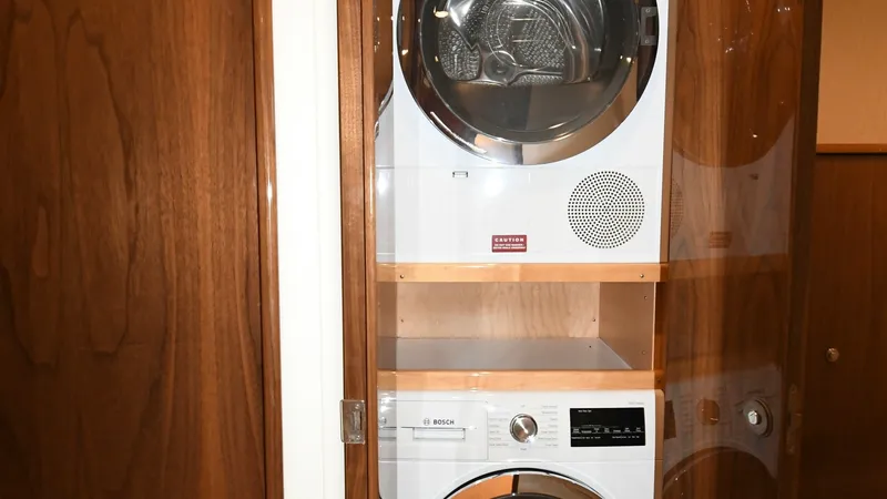 Slide: The Image of Laundry Station with Stackable Units This image showcases the laundry station aboard the 2020 Viking 58 Convertible, featuring high-end Bosch stackable washer and dryer units. Encased in rich wood cabinetry, the setup offers both functionality and elegance, seamlessly integrating into the ya - 6388309